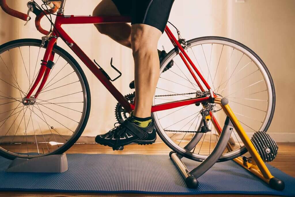 side view of man exercising with roller trainer on training mat and with front wheel support