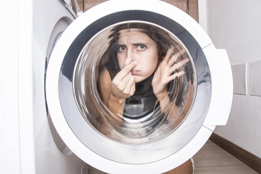 Woman holds her nose behind open washing machine door
