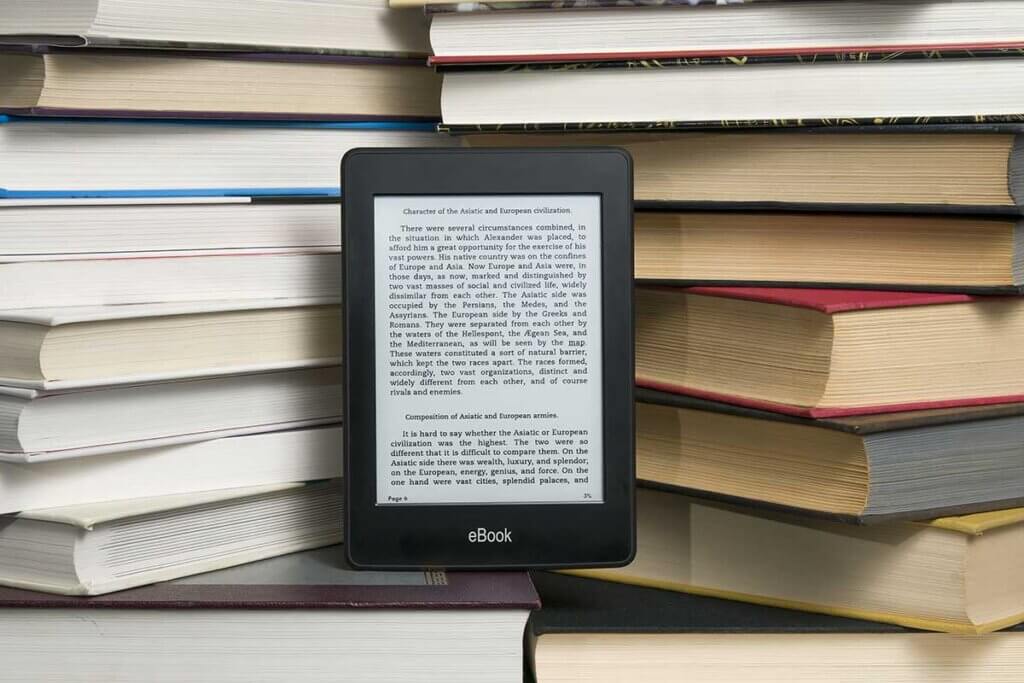 ebook reader stands in front of many stacked books