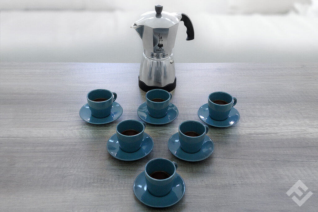 Bialetti moka timer on a table with six cups in front of it.
