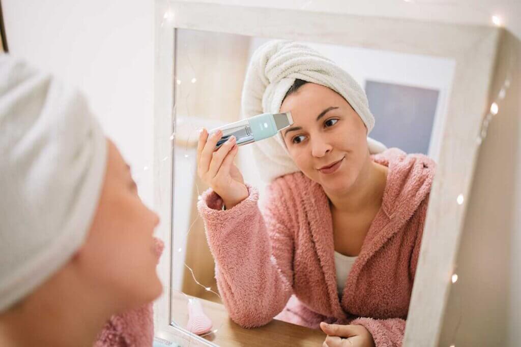woman uses cleansing brush before mirror
