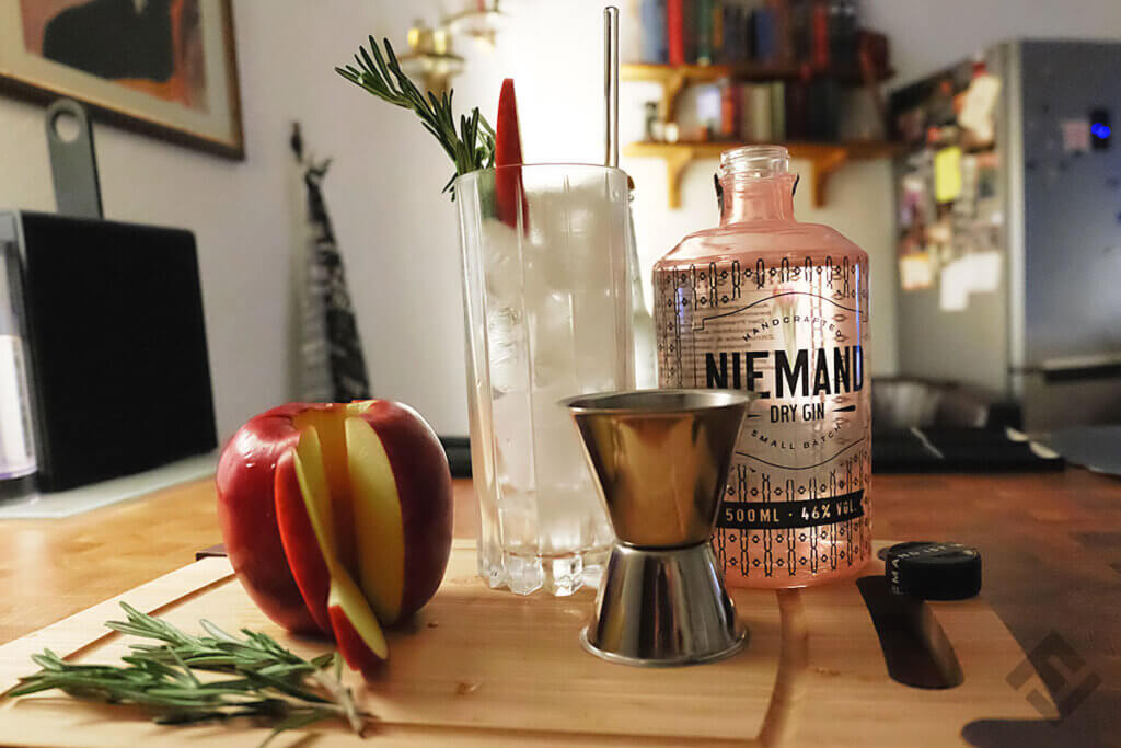 Niemand Gin with garnishes (apple, rosemary) on a wooden board.