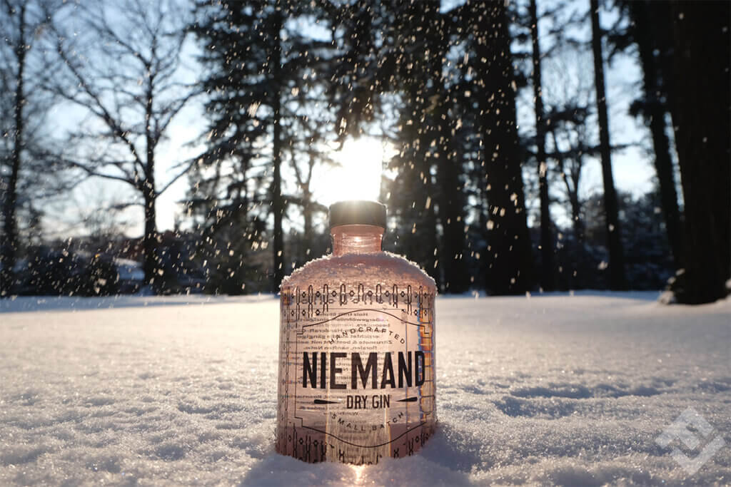 A bottle of Niemand Gin on a snow cover amidst trees.