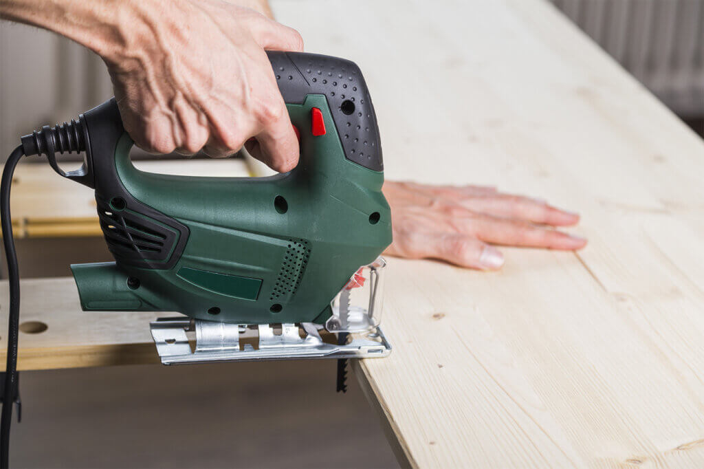 man saws wood board with jigsaw through