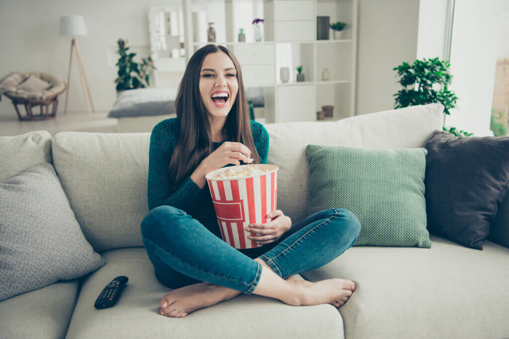  Woman sitting on sofa laughing and eating popcorn
