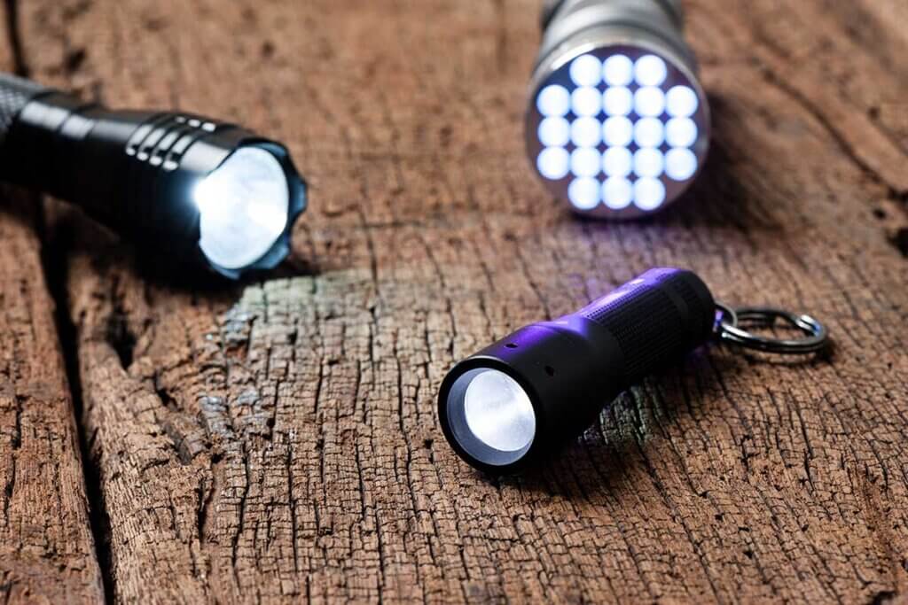 Three different flashlights lie switched on on a wooden table