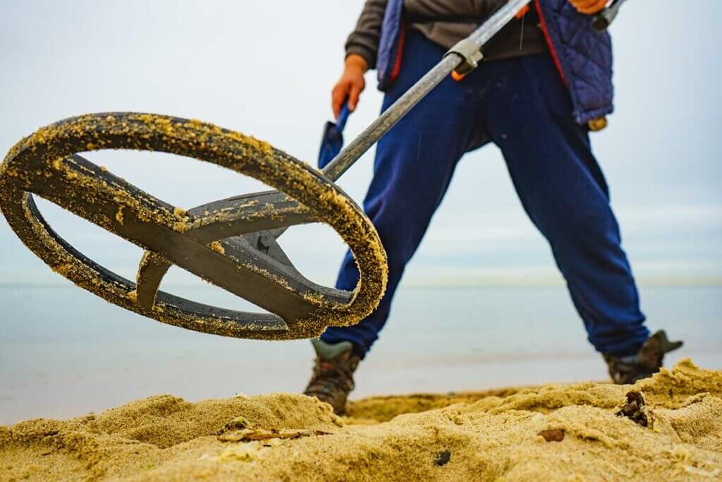 Man standing in sand with metal detector