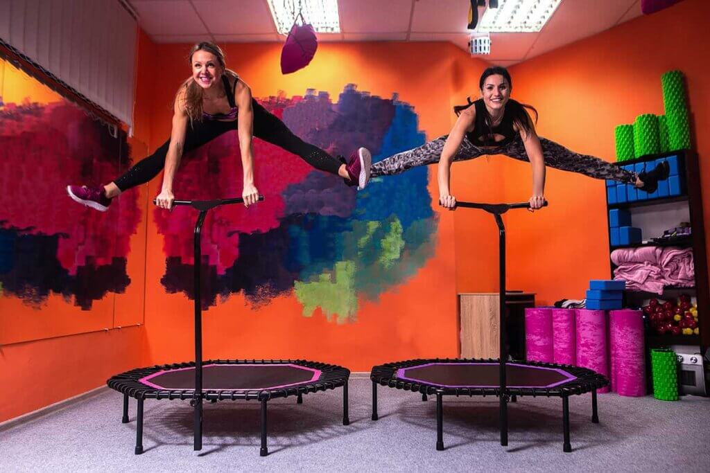 Two women jumping on a trampoline with a handhold