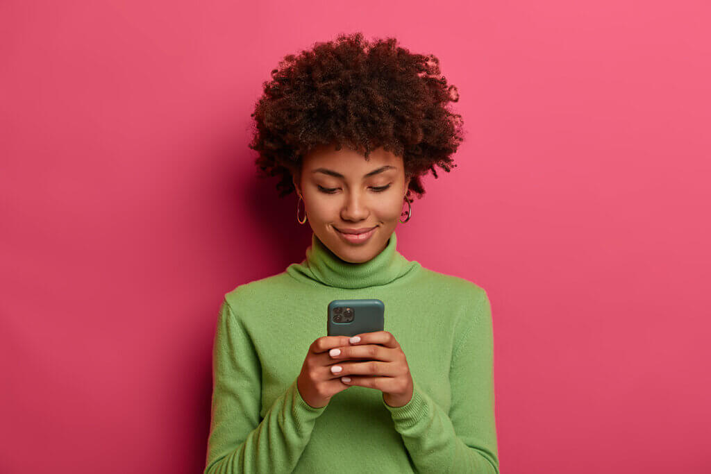 Woman with smartphone in front of pink wall