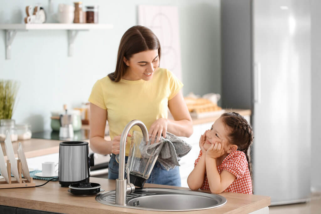 Mother cleans blender and child watches