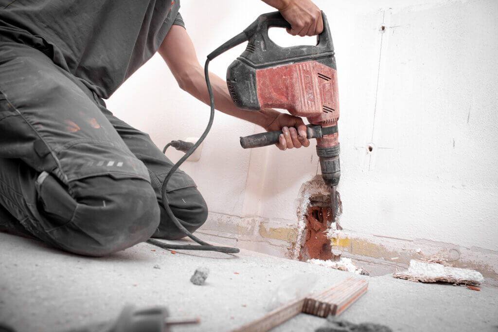 man uses rotary hammer on wall