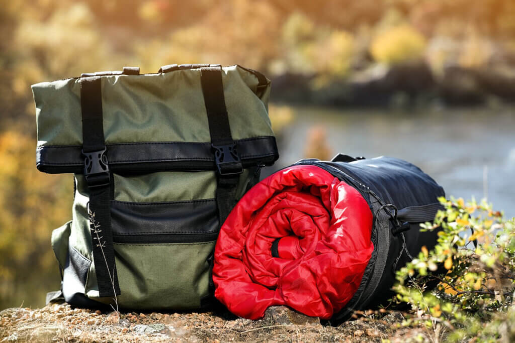 Backpack stands next to rolled-up sleeping bag in the great outdoors