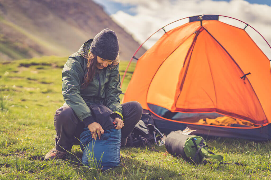 Person packs sleeping bag in a mountain landscape