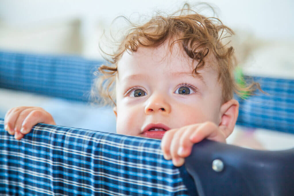 Baby in travel cot looks over the edge