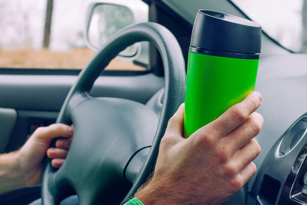 person holding travel mug while driving