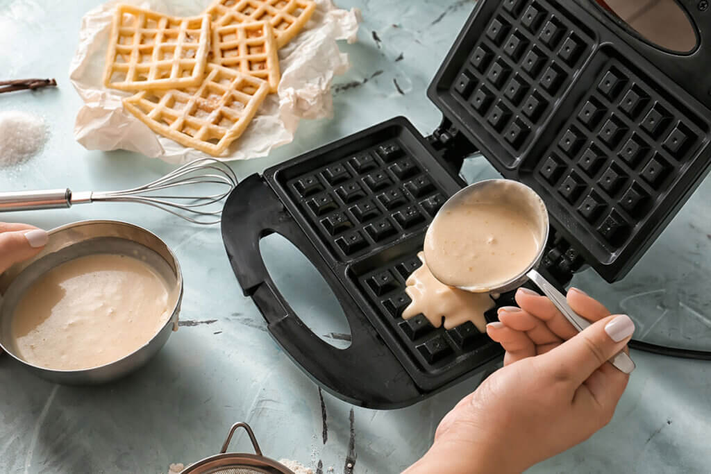 Woman pouring waffle batter into waffle iron