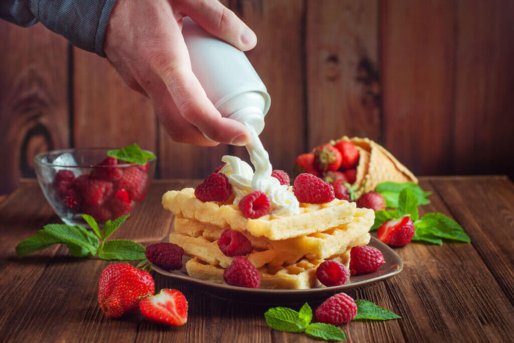 Person sprays cream on waffles with raspberries
